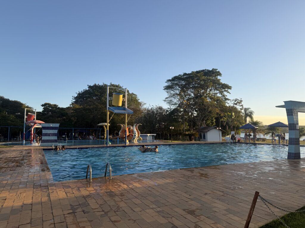 Piscina do clube ao entardecer, com crianças na água e o lago de Furnas ao fundo