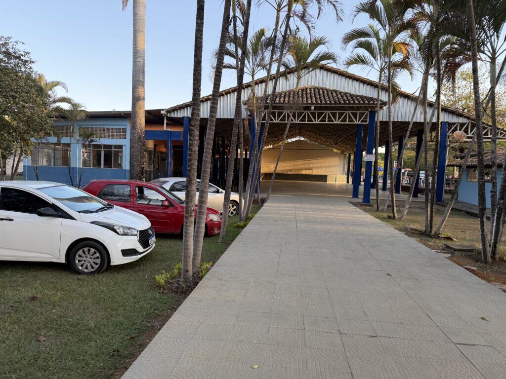 Salão coberto do clube visto da entrada, com estacionamento ao lado