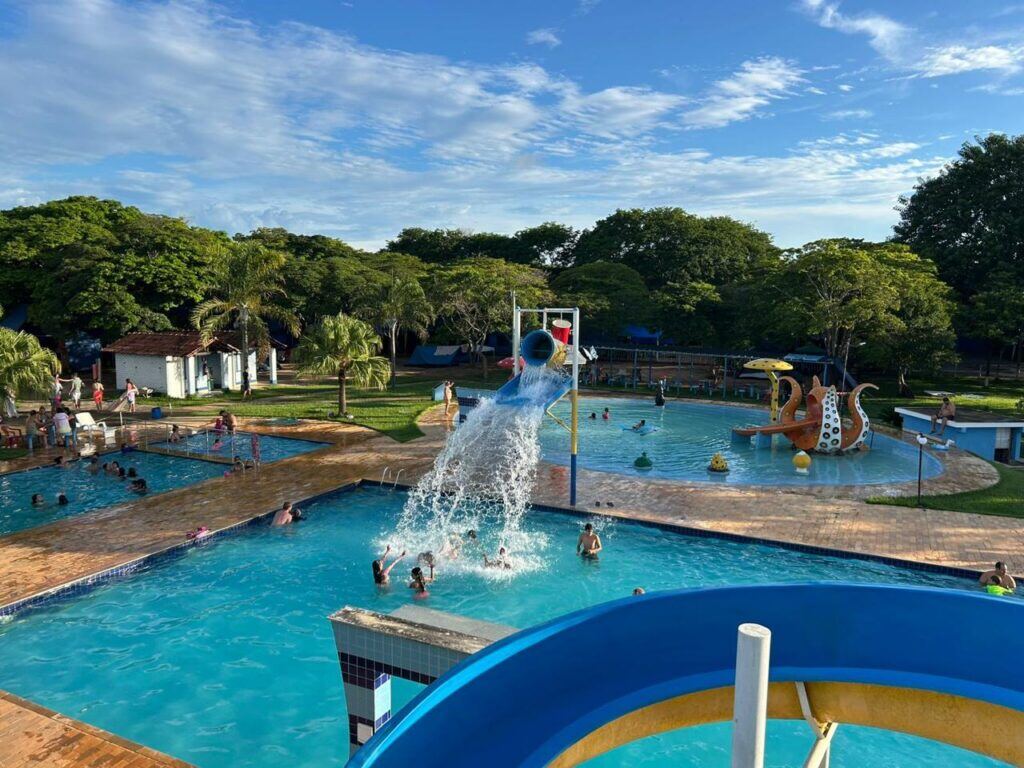 Vista geral das piscinas do clube com tobogã e famílias na água