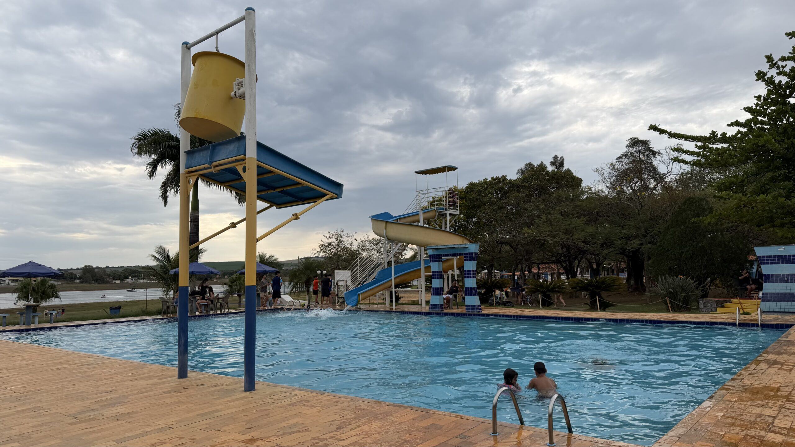 Piscina do clube com toboágua e crianças na água, com o lago ao fundo